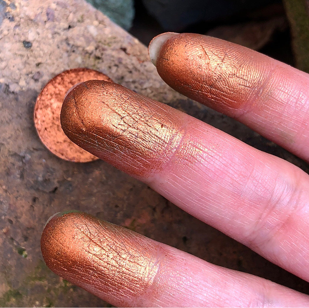 finger swatch of copper eyeshadow in front of some rocks